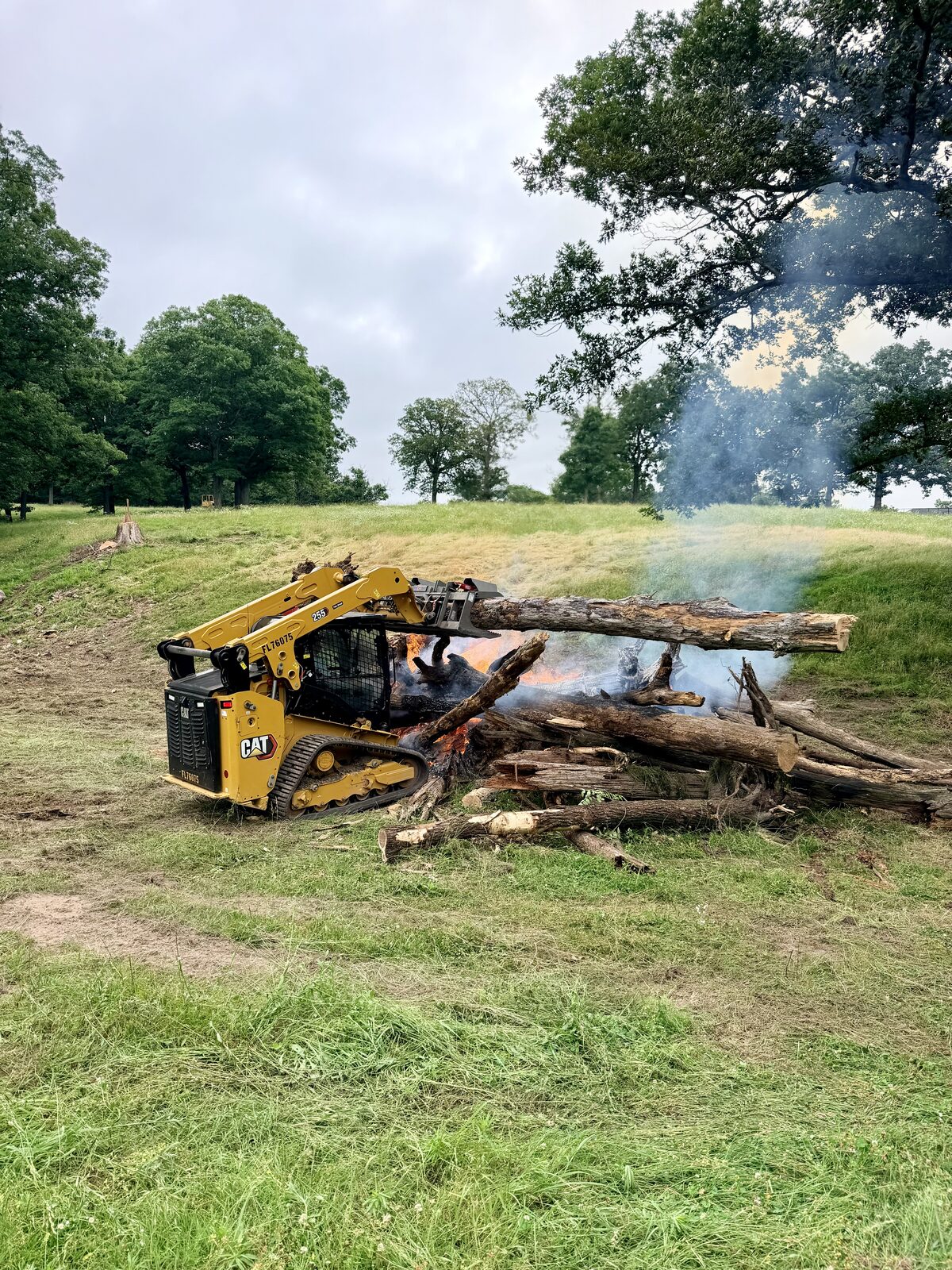 Skid steer stacking cleared trees on a burn pile in a Northwest Arkansas pasture
