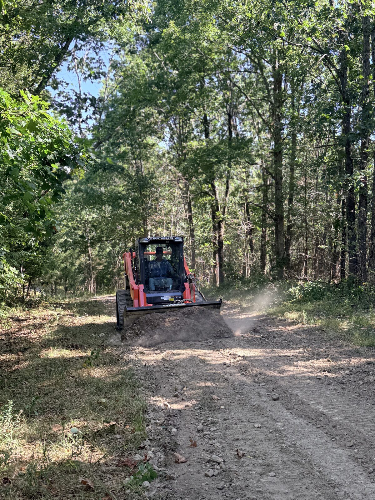 Skid steer regrading a rutted road through the woods