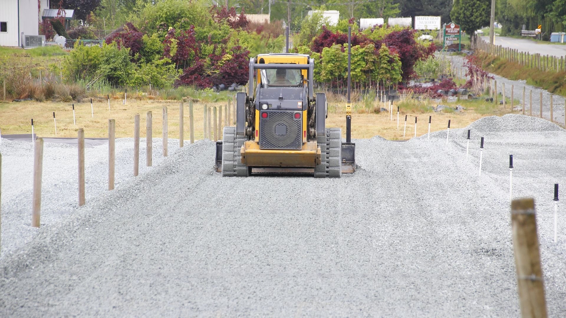 Yellow skid steer loader working on gravel road with wooden posts
