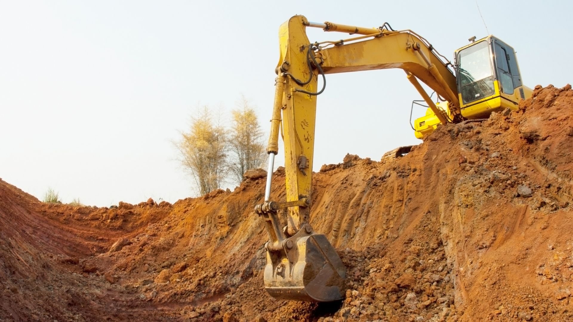 Yellow excavator digging earth on construction site with reddish soil