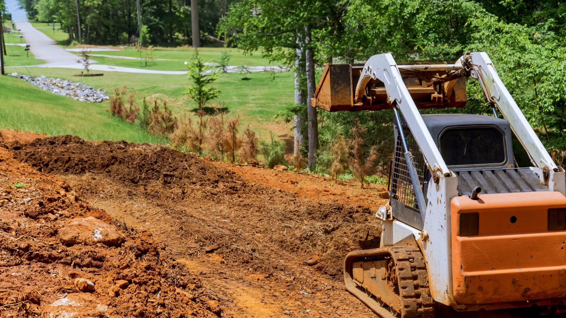Tracked skid steer loader working on dirt excavation near landscaped area