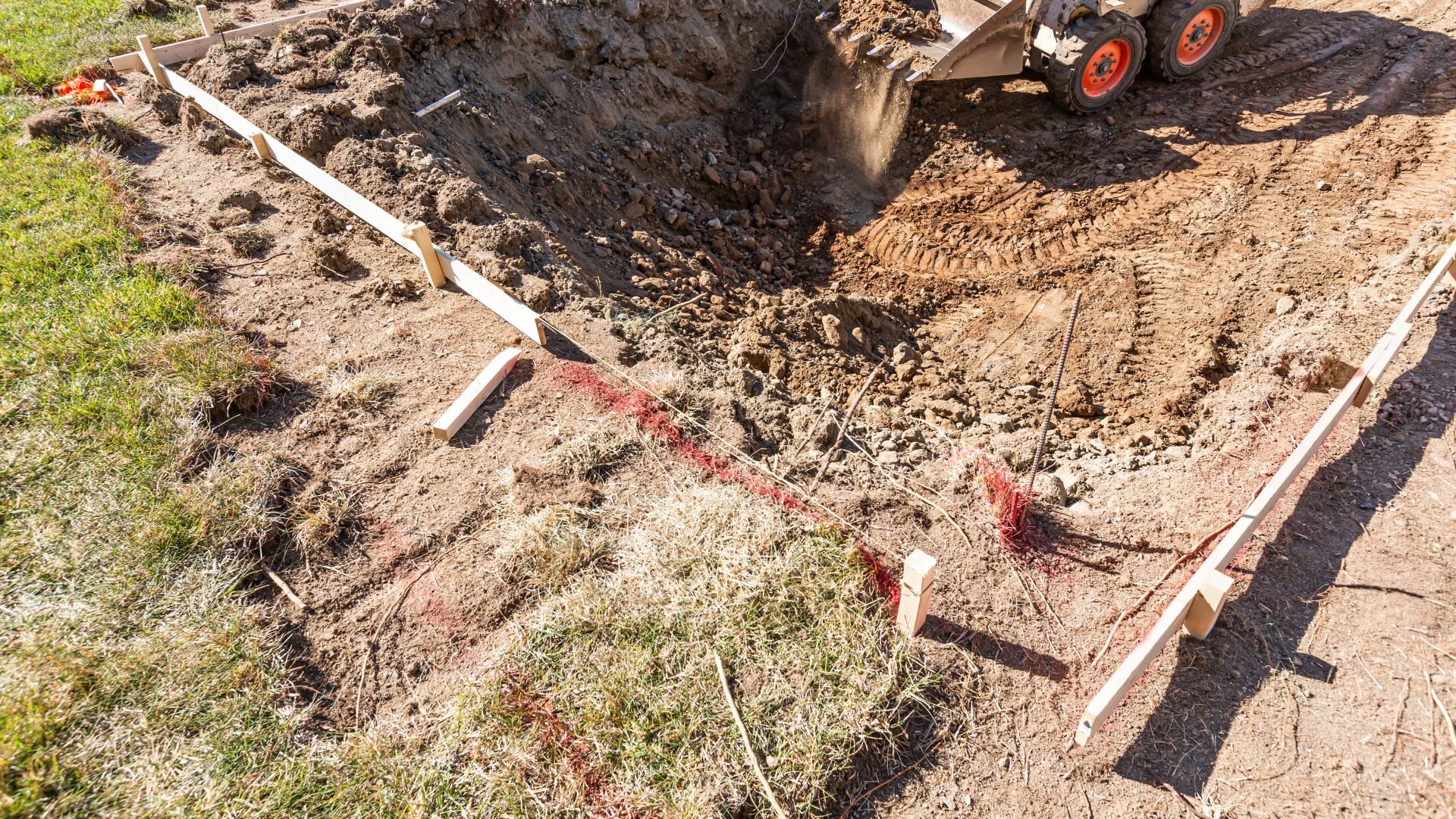 Construction site with deep excavation, wooden markers, and heavy machinery