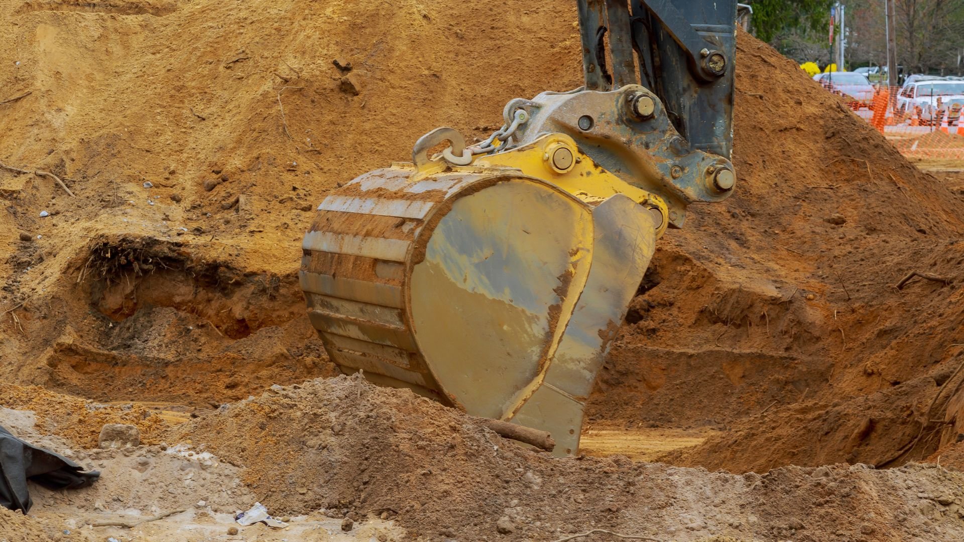 Yellow excavator bucket digging into sandy construction site ground